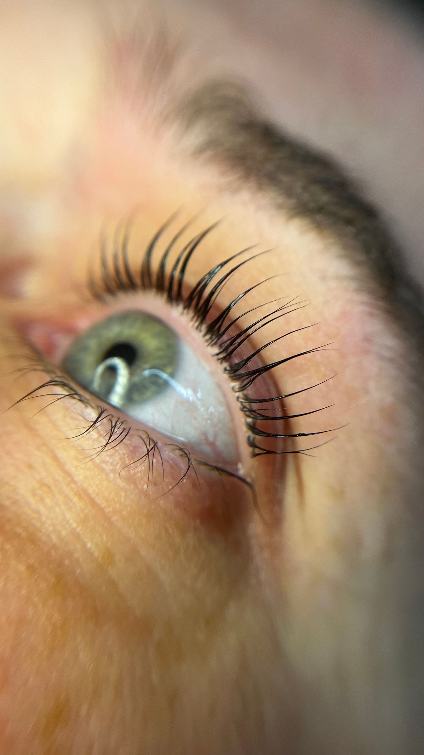 Geliftete Wimpern über einem grünen Auge, seitlich fotografiert